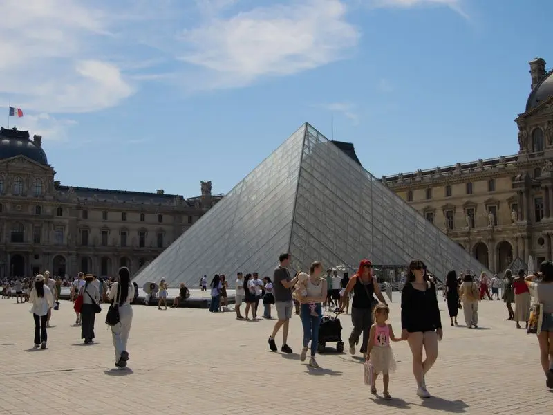 Visitors crossing the Louvre courtyard in front of the glass pyramid in Paris