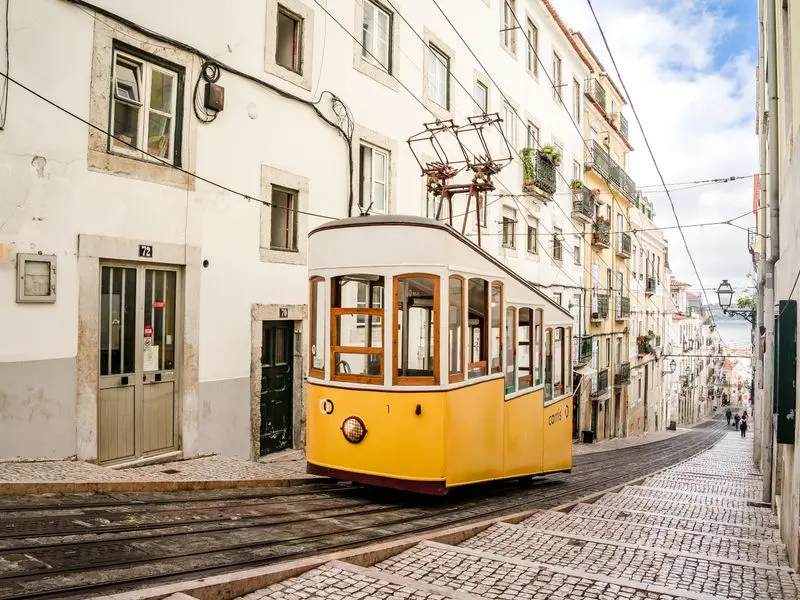 A yellow tram climbing a narrow street in Lisbon